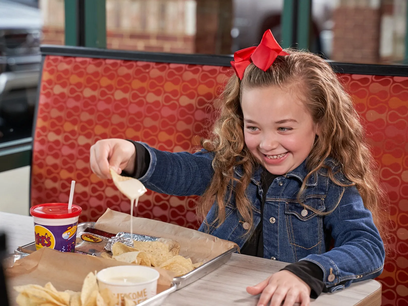 Girl with red bow dipping chip in queso — the perfect cheese pull